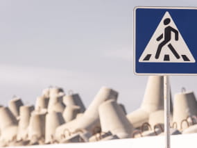 Знак пешеходного перехода на фоне бетонных блоков.